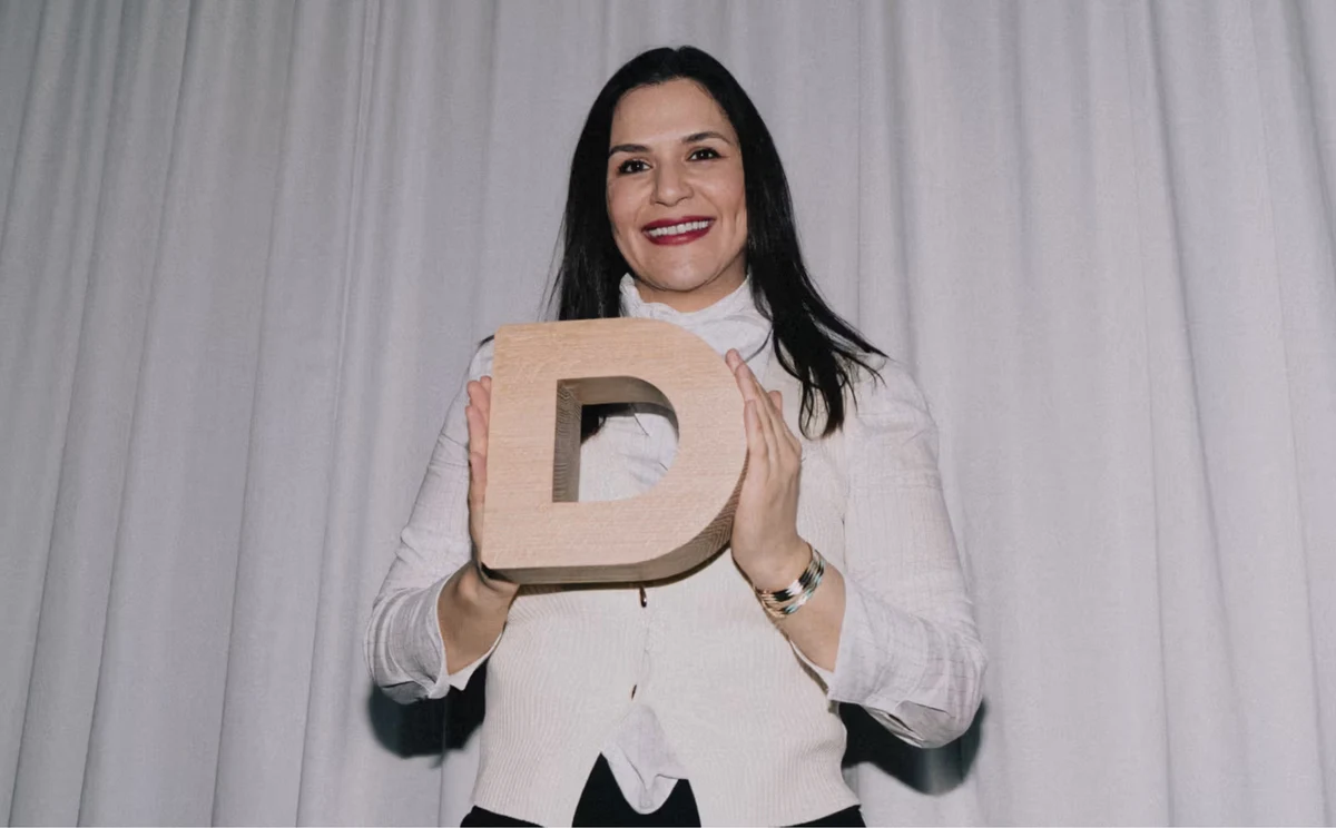 Diana Saleh holding the wooden Danish Design Award trophy in front of pale curtains